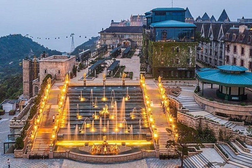 A historic fountain with water jets, surrounded by stone steps and illuminated by lights. 3