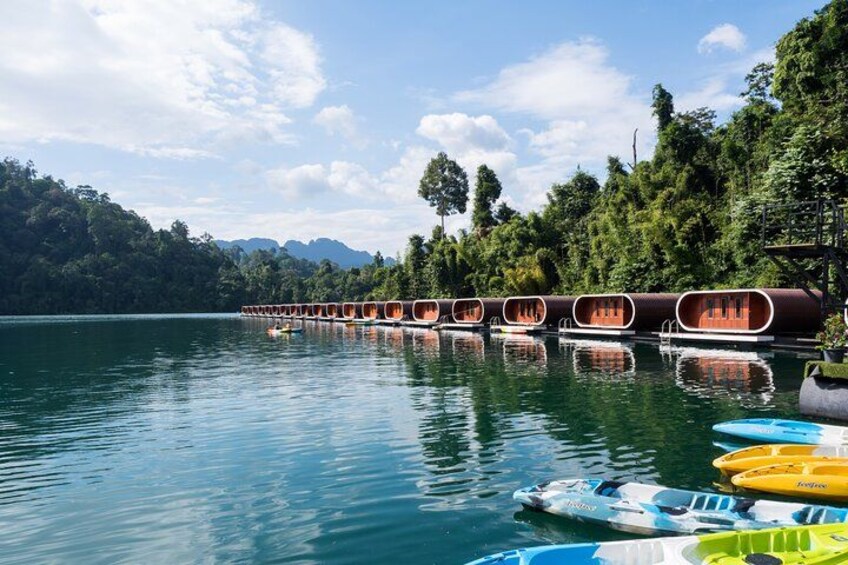 Une rangée de cabanes en bois flottantes sur un lac paisible, entourée d’une végétation luxuriante et avec des montagnes en arrière-plan. 3