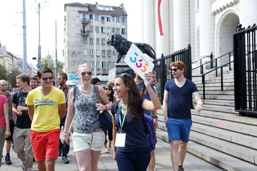 Een groep mensen loopt over een straat in de stad, met een standbeeld en gebouwen op de achtergrond. 3