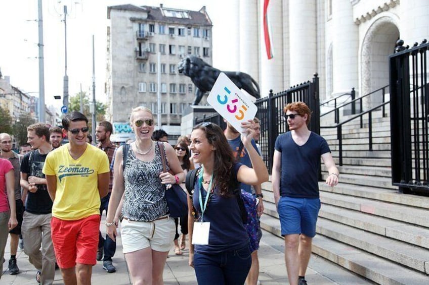 Un grupo de personas caminando por una calle de la ciudad, con una estatua y edificios al fondo. 3