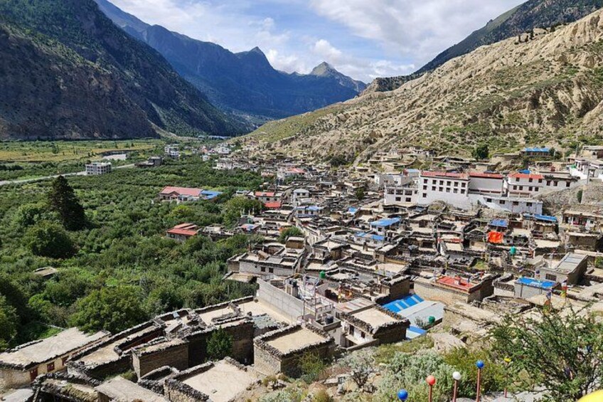 Un pueblo montañoso con casas tradicionales, un edificio destacado con techo rojo y un valle cubierto de vegetación. 4