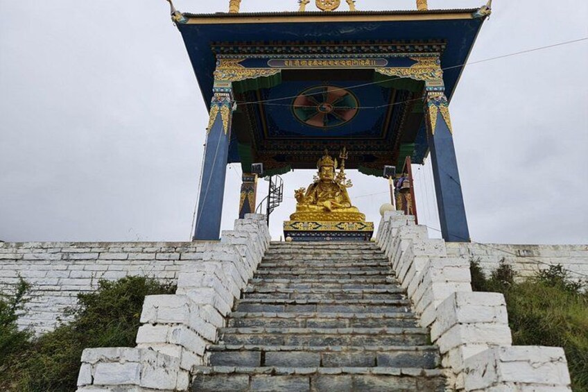 Una estatua dorada en la cima de una escalera de piedra que conduce a una estructura con techo azul y un símbolo de rueda. 2