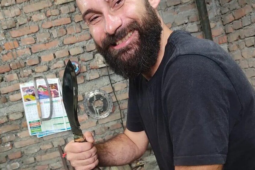 A person holding a knife with a black handle and a metallic blade, standing in front of a brick wall with a calendar and a glass object on the ground. 4