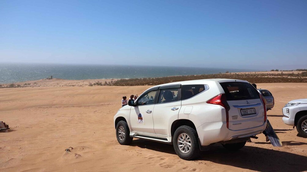 A white SUV parked on a sandy beach with a clear view of the ocean in the background. 4