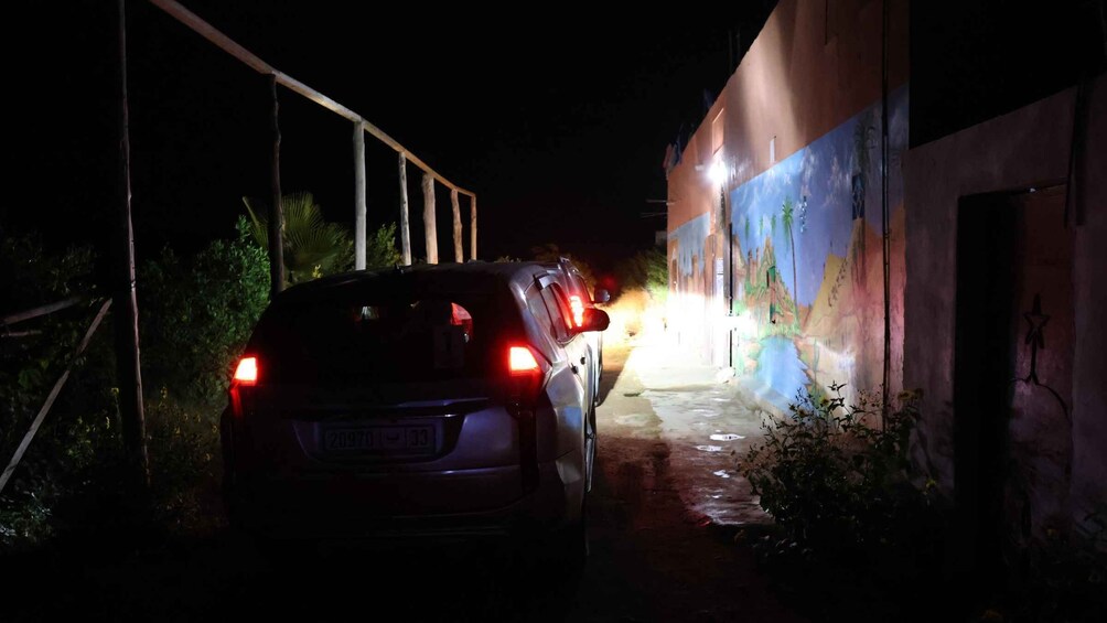 A car parked in a dimly lit alleyway with a mural on the wall. 3
