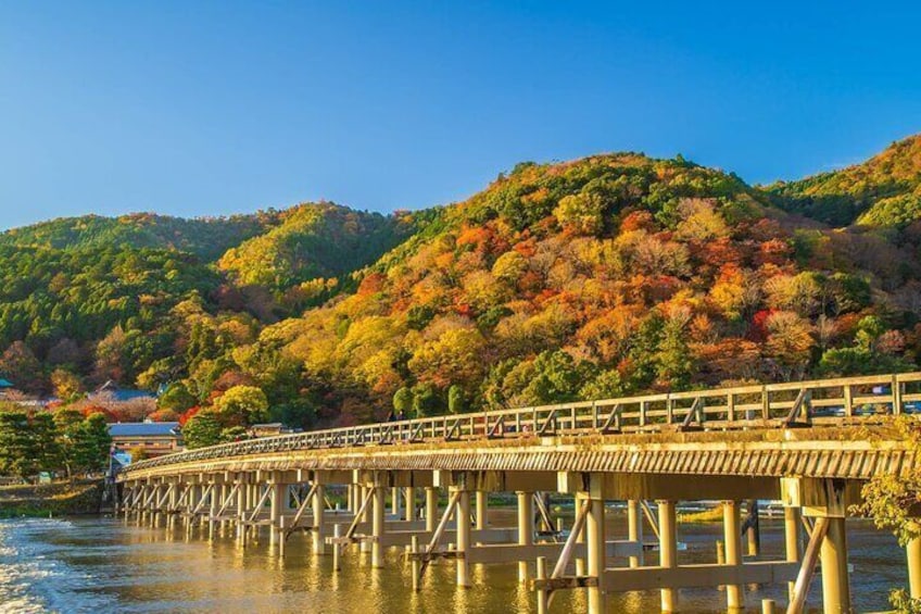 A wooden bridge over water with autumn foliage on hills in the background. 4