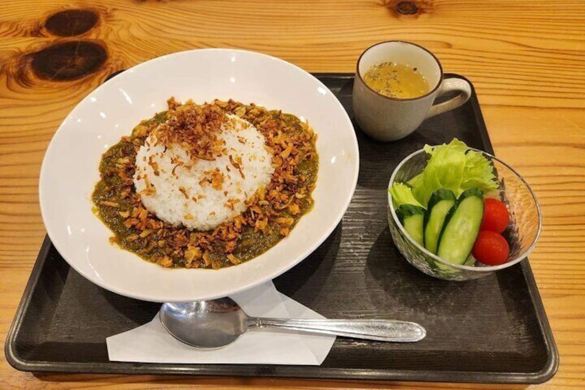 A plate of rice topped with a green sauce and fried onions, a small bowl of salad, and a cup of soup on a wooden table. 3