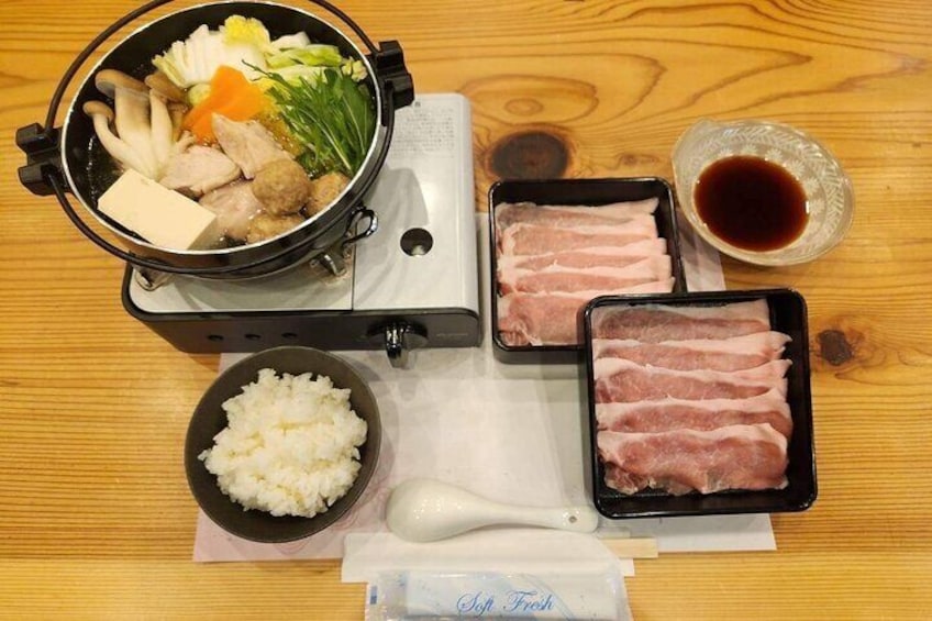 A meal setup with a pot of soup, rice, sliced meat, and a bowl of soy sauce on a wooden table. 5