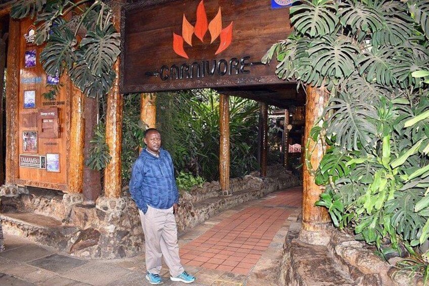 A man standing in front of a wooden sign with a flame logo and the word 'CARNIVORE' on it. 5