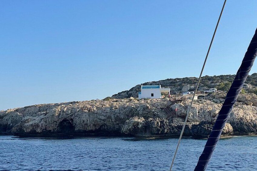 A rocky coastline with a white building on a hill, a clear blue sky, and calm sea. 2