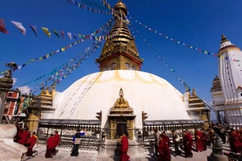 A large white temple with a golden spire, surrounded by people in red robes. 4