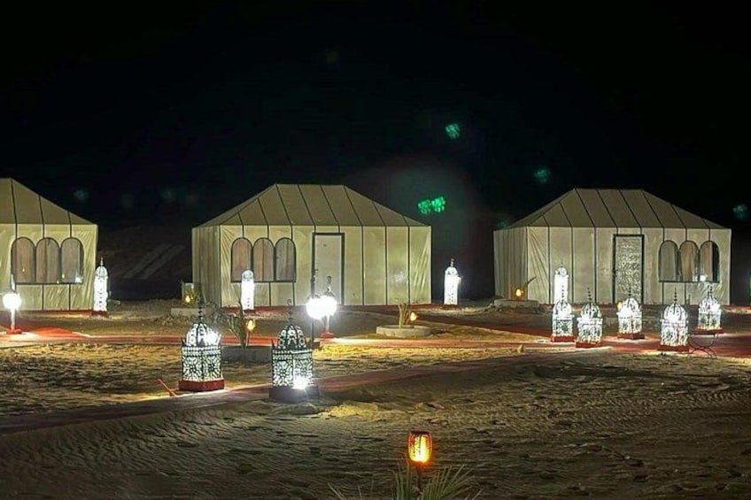 A series of tents with illuminated windows and decorative lanterns in a desert setting. 2