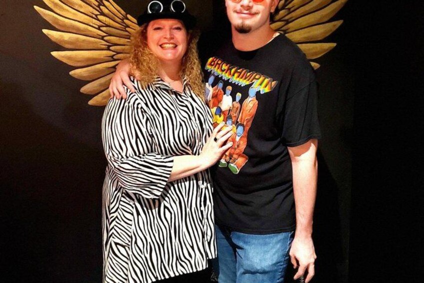 A person in a zebra-striped dress with a winged headpiece and another person in a black t-shirt with colorful graphics. 5
