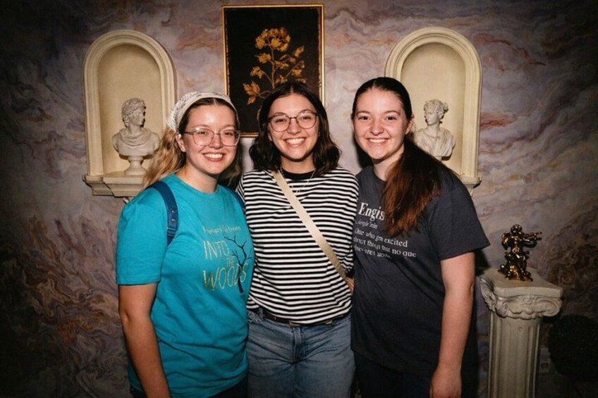 Three people standing in front of a marble wall with busts and a framed painting. 4