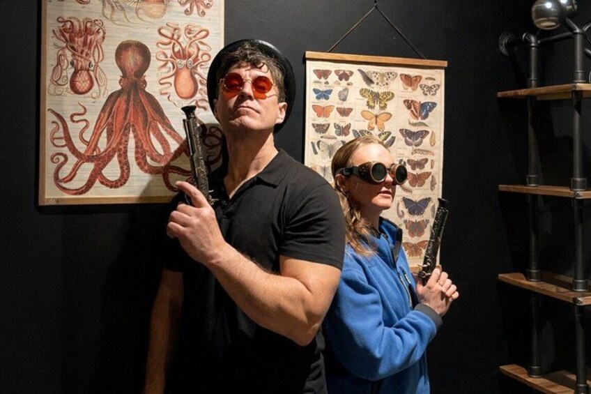 Two people holding guns in front of a wall with butterfly illustrations. 1