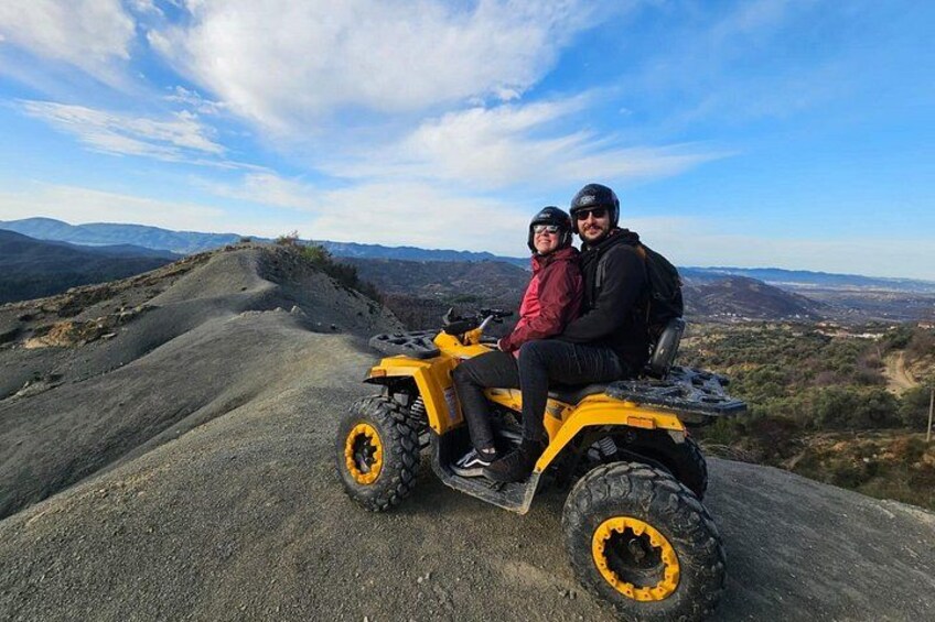 Two people on a yellow ATV on a dirt road with a mountainous landscape in the background. 4