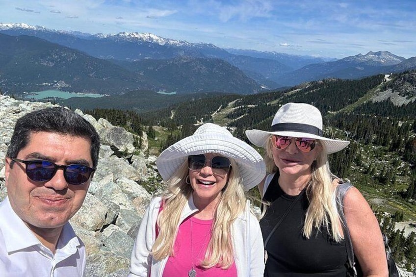 Tres personas de pie en una montaña, con un lago y montañas nevadas al fondo. 5