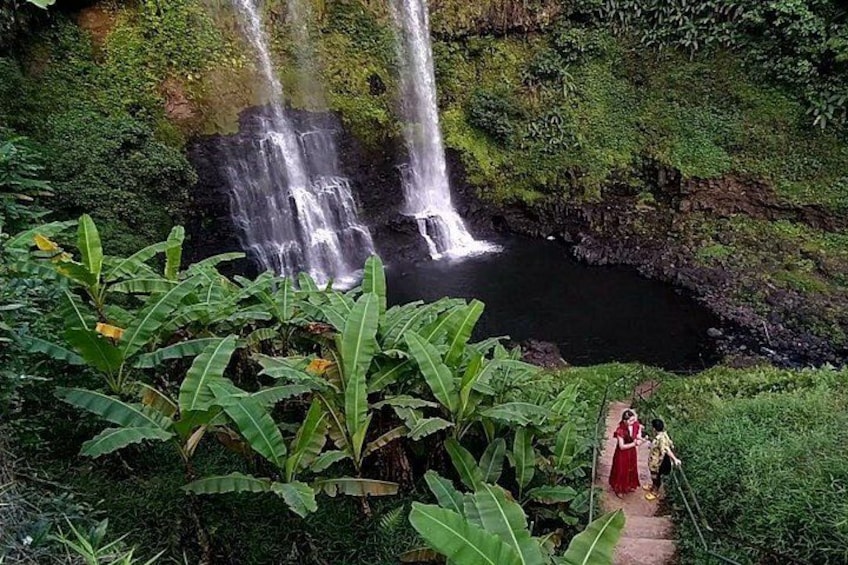A waterfall, lush greenery, and a person in a red dress walking on a path. 3