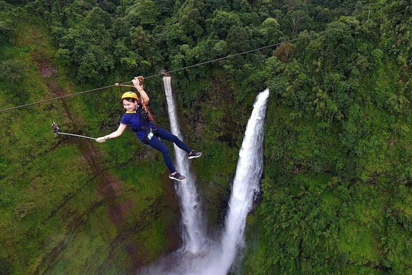 A person zip-lining over a waterfall, surrounded by lush greenery. 1