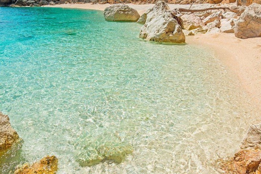 A clear turquoise sea, sandy beach, and large rocks. 3