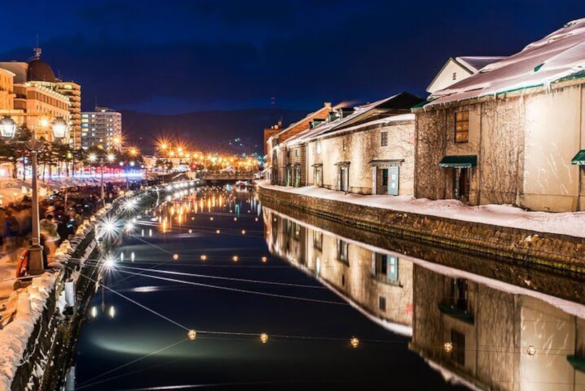 A nighttime canal with buildings on one side and a cityscape in the background. 2