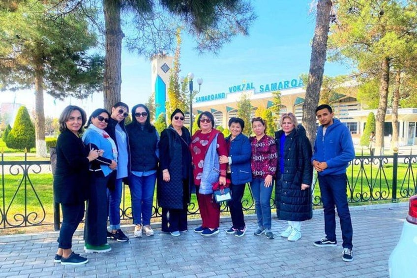 A group of people standing in a park with trees and a building in the background. 3