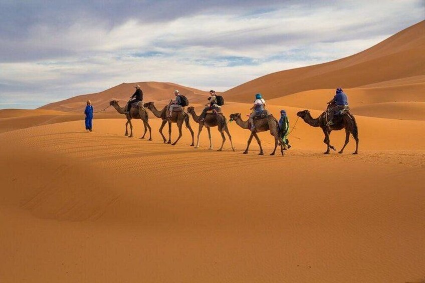 A group of people riding camels across a desert landscape with sand dunes. 1