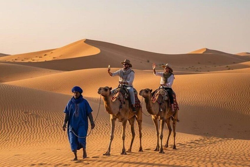 Three people riding camels in a desert with sand dunes in the background. 4