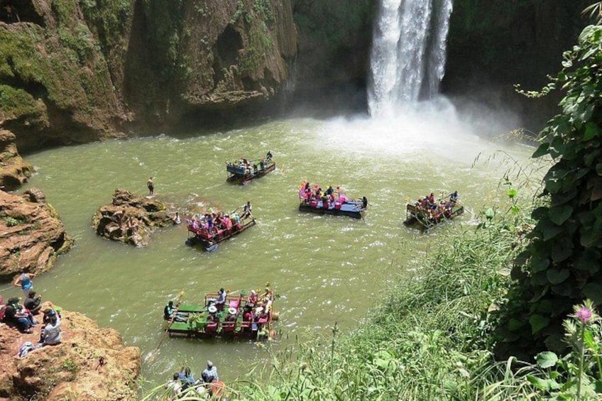 Een rivier met diverse boten vol passagiers, omringd door rotswanden en een waterval. 5