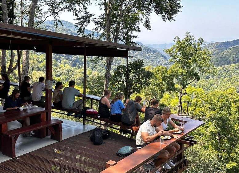 People dining at an outdoor table with a scenic view of a forested mountain range. 5