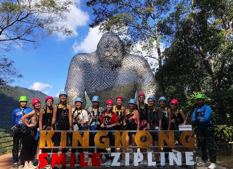 A group of people in helmets and harnesses standing in front of a large sculpture with the text "KINGKONG SMILE ZIPLINE". 1