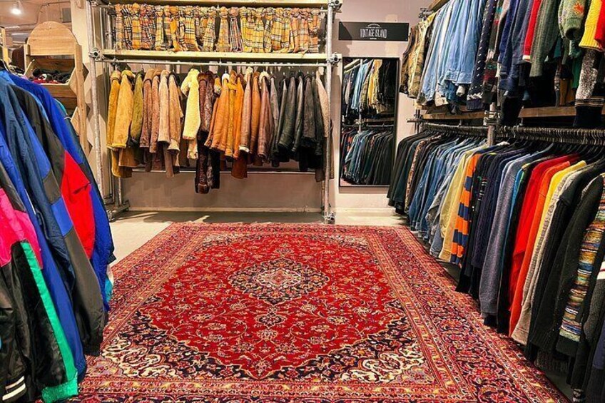 A clothing store with racks of clothes and a large red patterned carpet. 3