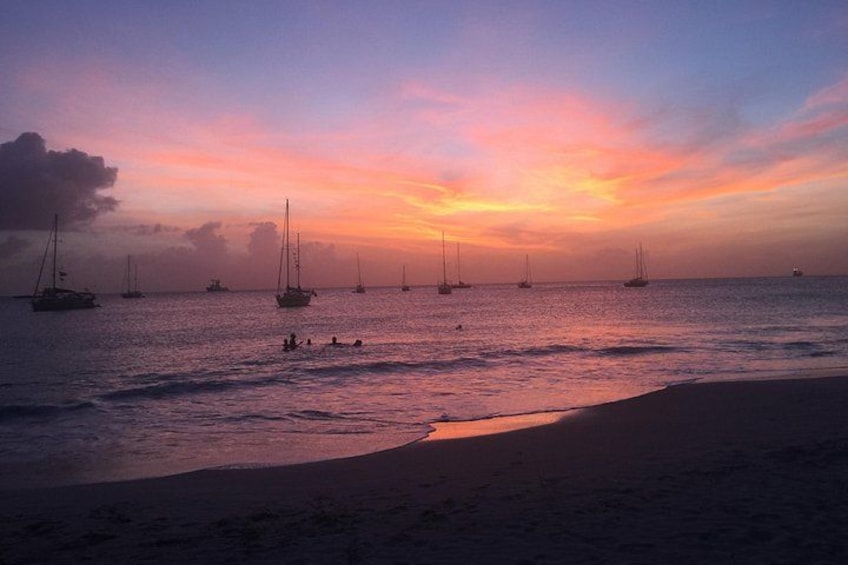 A sunset over a beach with sailboats and people in the water. 2