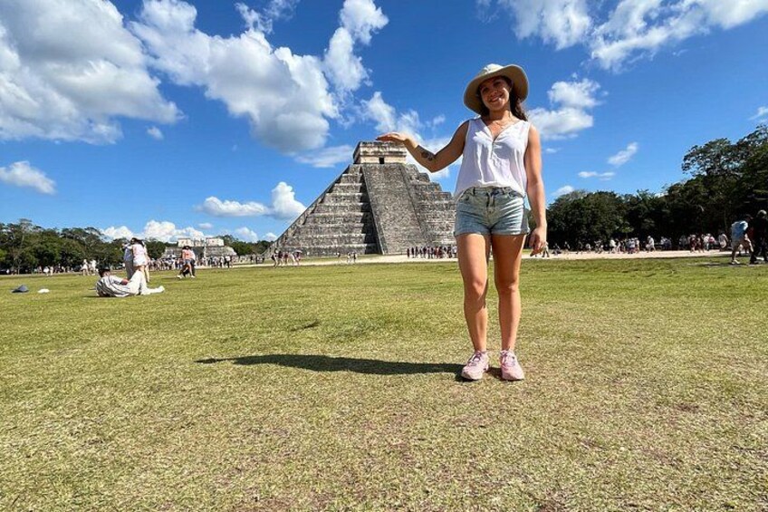 Una persona de pie frente a una gran estructura piramidal en un área verde, con cielo despejado. 2