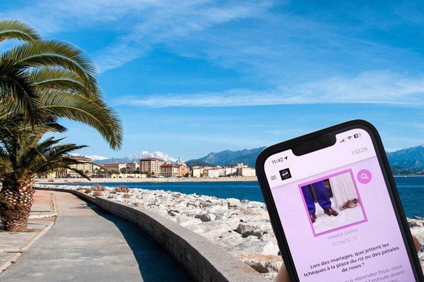 Un teléfono inteligente mostrando una foto de una playa con una palmera, un muro de piedra y edificios al fondo. 5