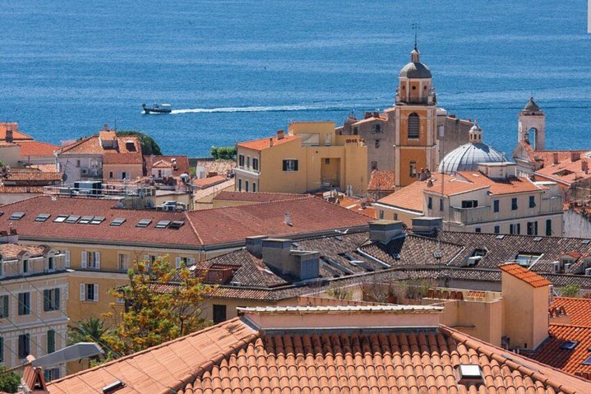 Un paisaje urbano costero con edificios de techo terracota, una iglesia destacada con cúpula y un mar azul cristalino. 4
