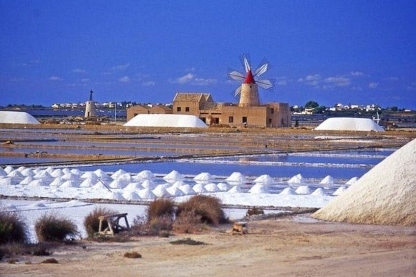 A windmill, salt pans, and a building in a coastal landscape. 2