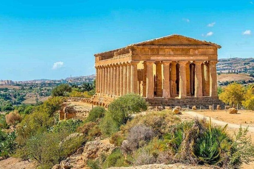An ancient Greek temple with columns, set against a hilly landscape with sparse vegetation. 3