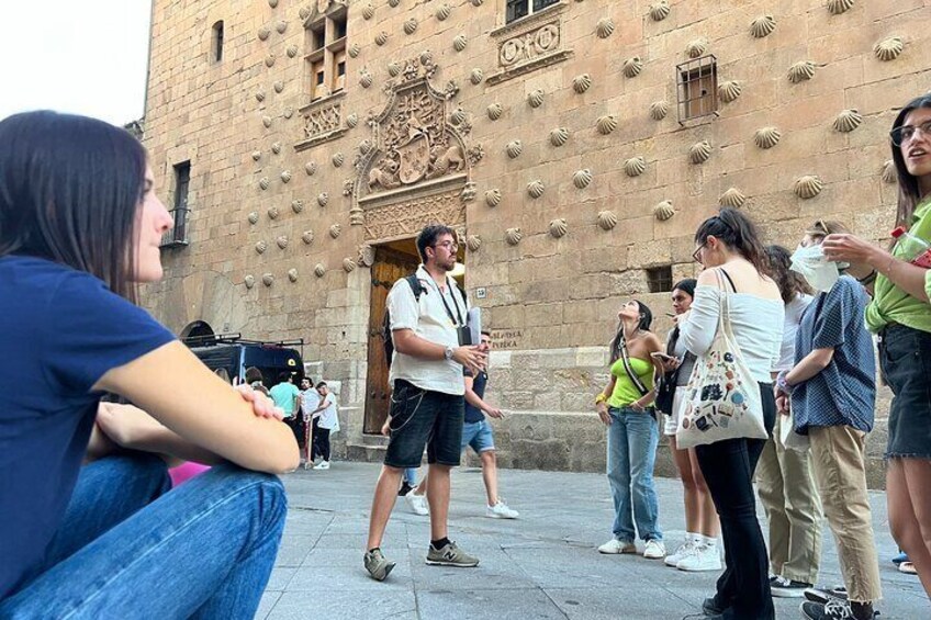 People standing and walking in front of a historic building with a scalloped stone facade. 4