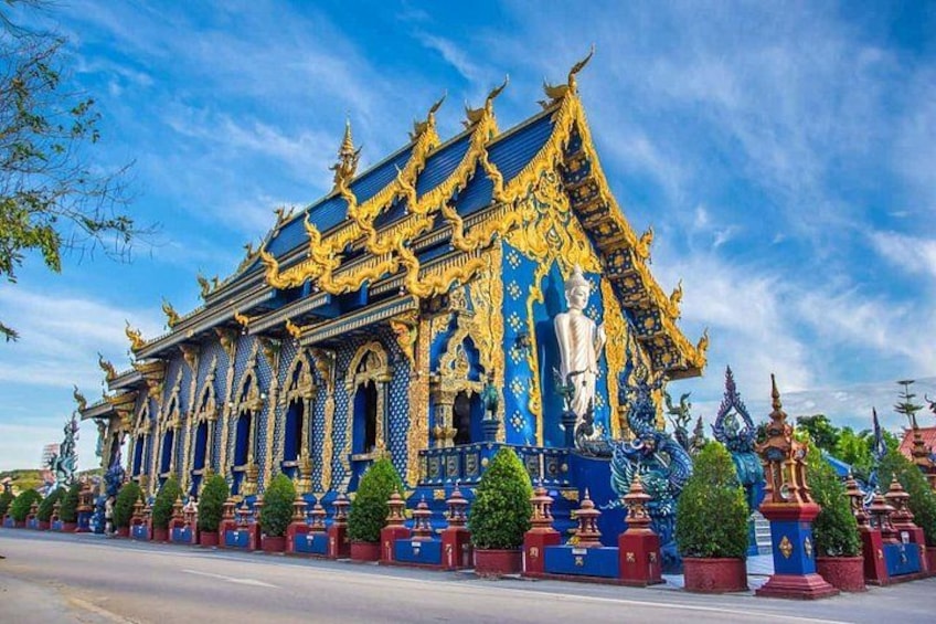 Een statig tempel met ingewikkelde gouden en blauwe decoraties, een groot centraal standbeeld en weelderige begroeiing. 5