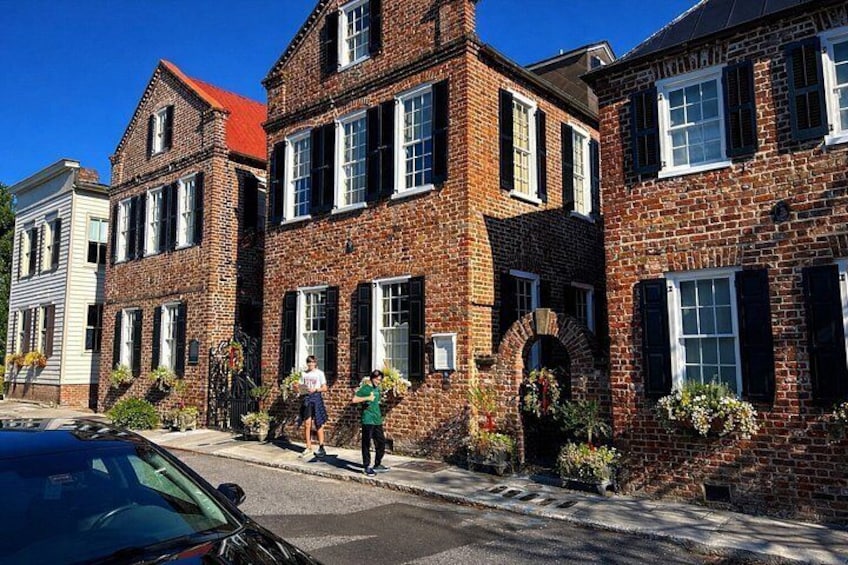 A row of brick buildings with white window shutters, a clear blue sky, and a parked car. 4