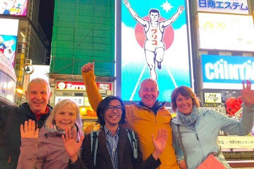 A group of people posing in front of a large digital advertisement with a wrestler. 1
