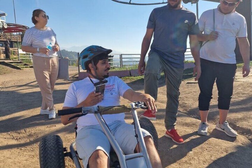 A person in a wheelchair using a smartphone, with others walking around in a park-like setting. 5