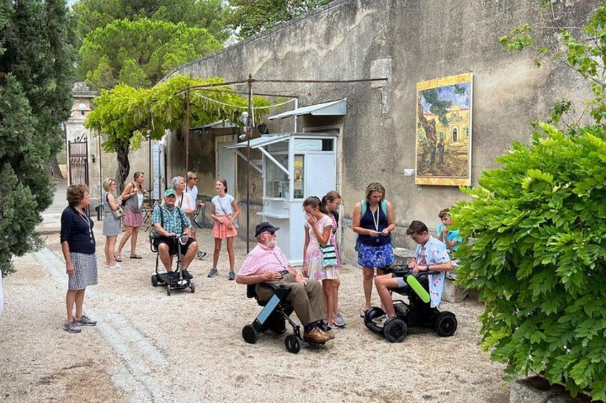 Un gruppo di persone in un cortile con un edificio, un albero e un quadro appeso al muro. 5