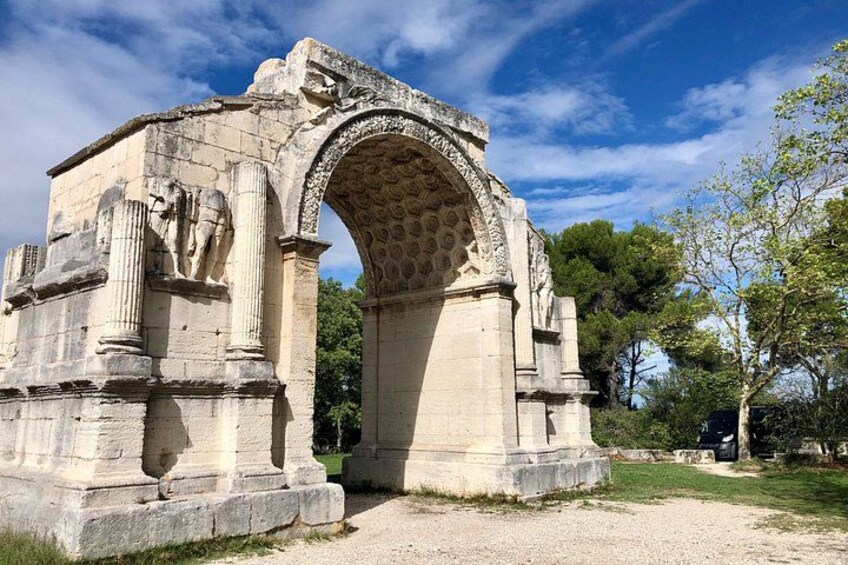 Un'antica arcata in pietra con colonne, circondata da alberi e un cielo sereno. 3