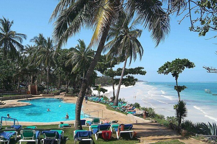 A pool surrounded by palm trees, a beach, and a clear blue sky. 5