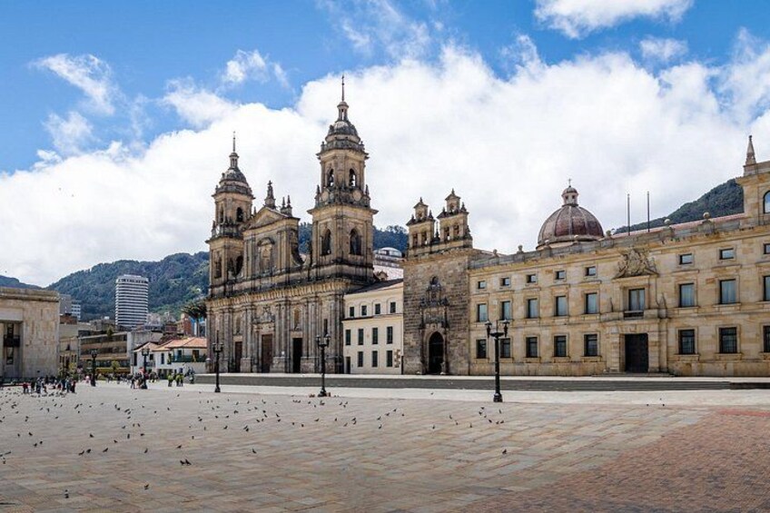 A historic cathedral with two towers, a plaza with pigeons, and a mountain in the background. 4