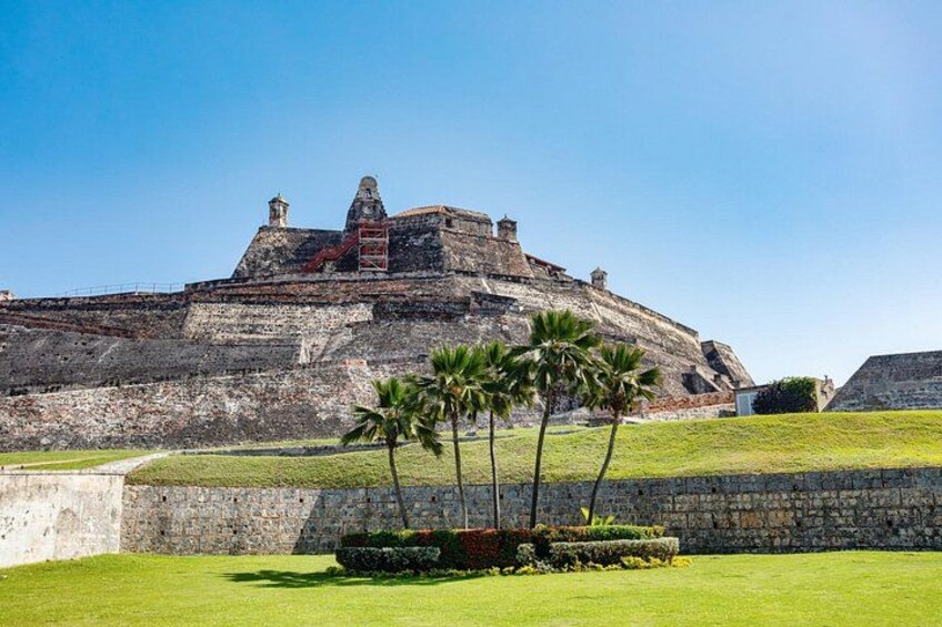 A historic fort with a grassy foreground and palm trees. 1