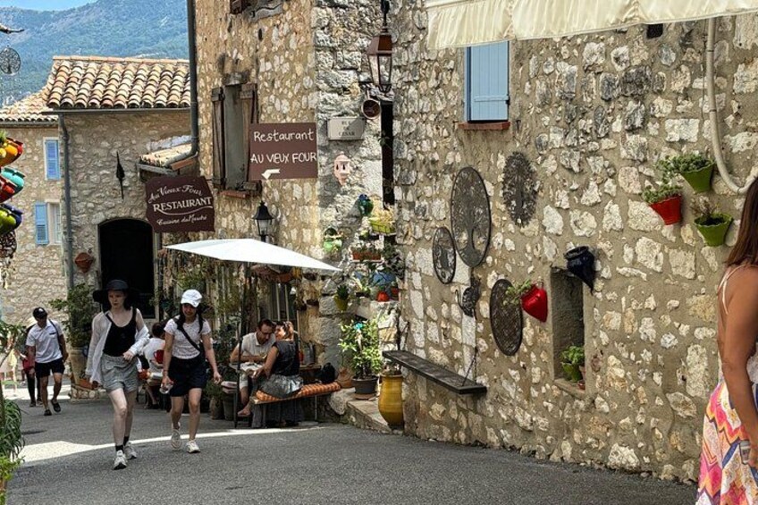 A street with stone buildings, outdoor seating, and signs for a restaurant. 1