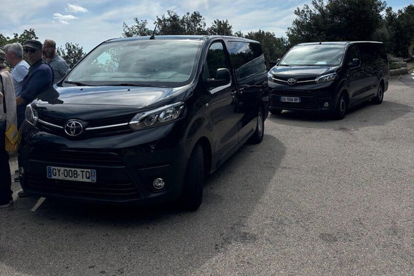 Two black Toyota vans parked in a lot with people standing nearby. 5